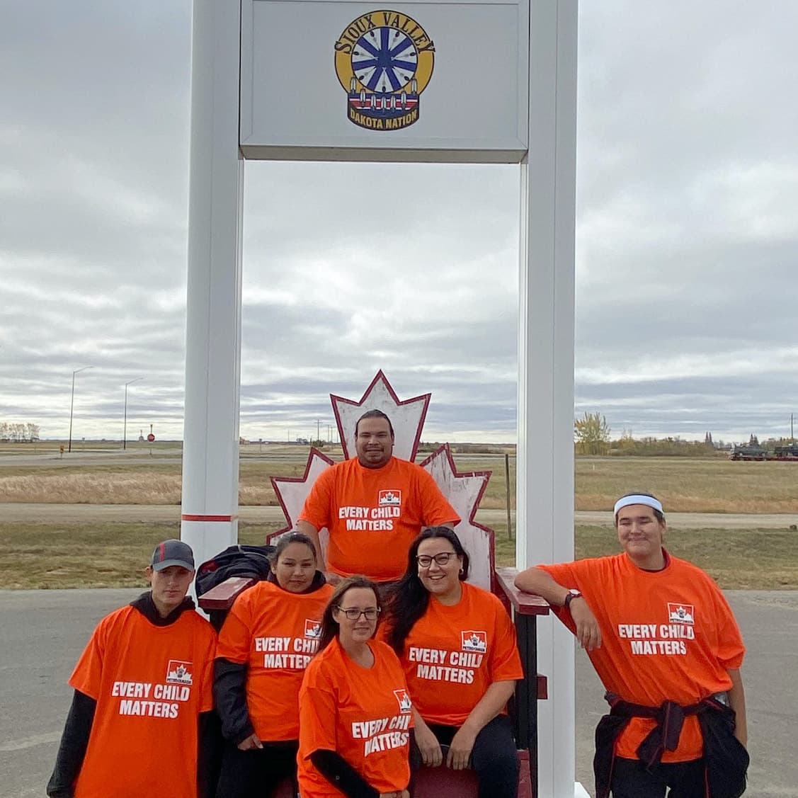 Six members of the Sioux Valley Dakota Nation pose in front of a Petro-Canada sign wearing orange shirts that read, Every Child Matters.