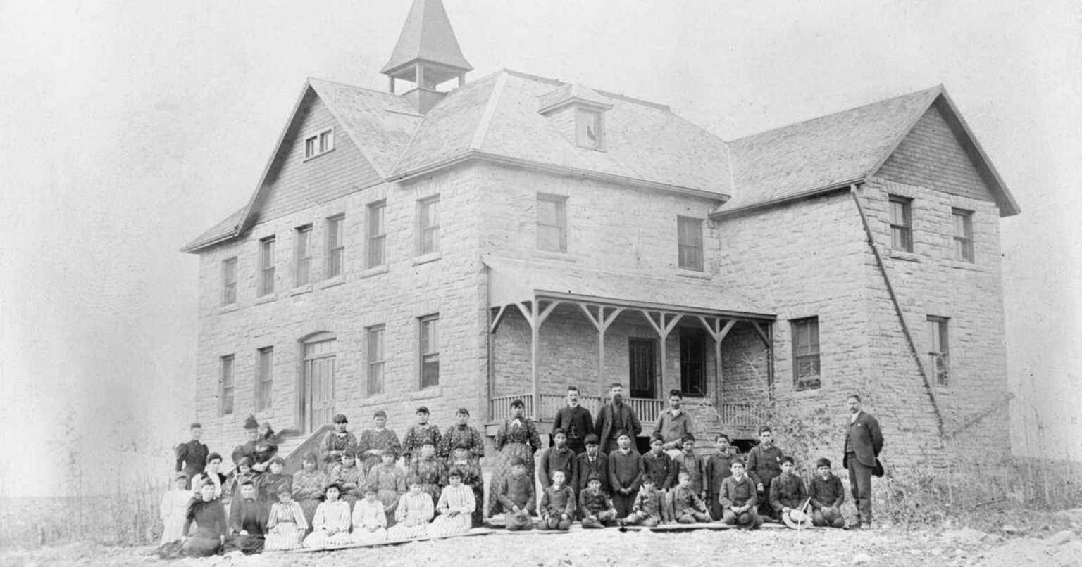 Vintage photo en noir et blanc d'un bâtiment institutionnel avec des étudiants et du personnel posés devant le bâtiment.
