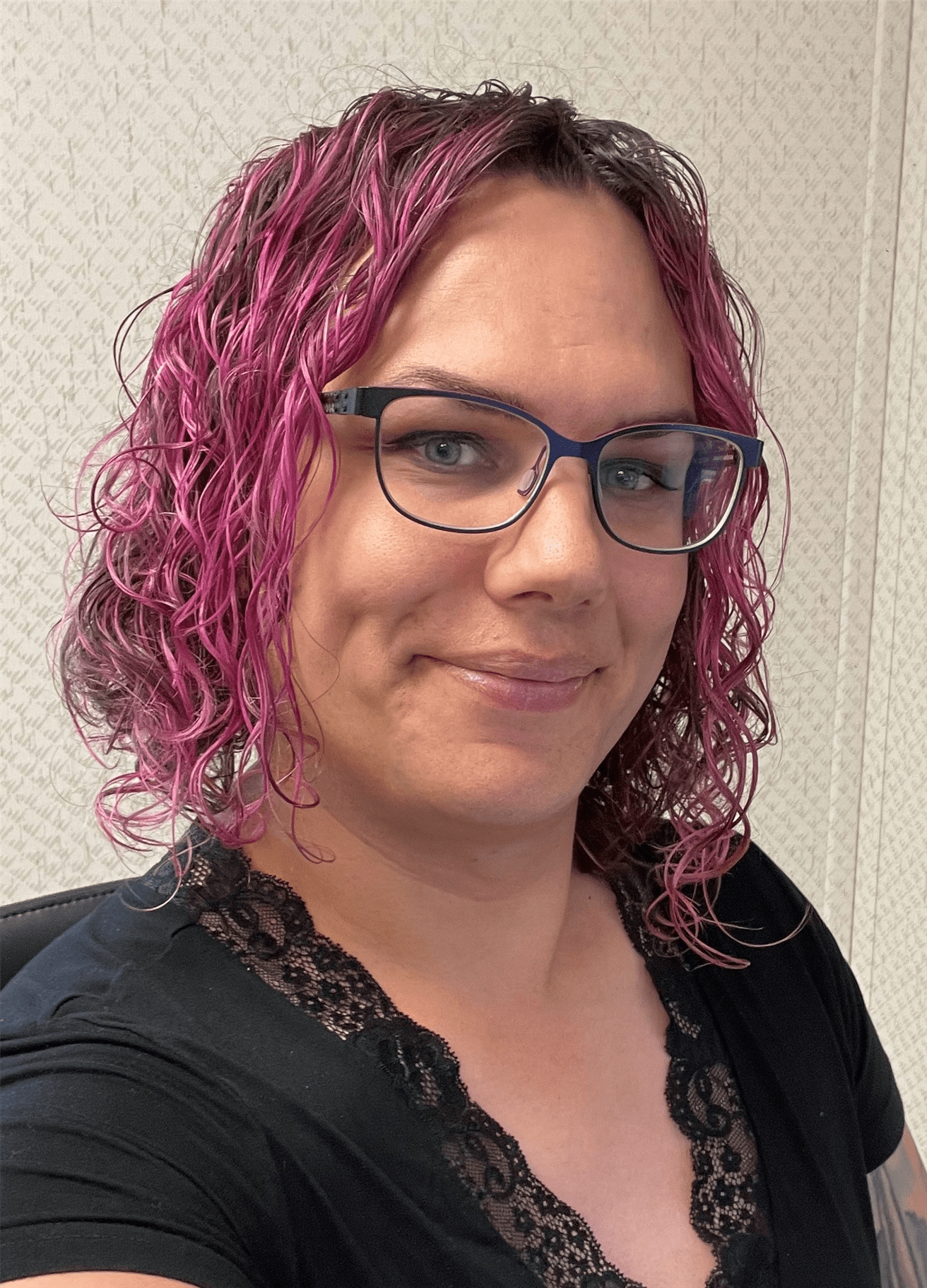 A woman with pink hair and glasses wearing a black shirt.