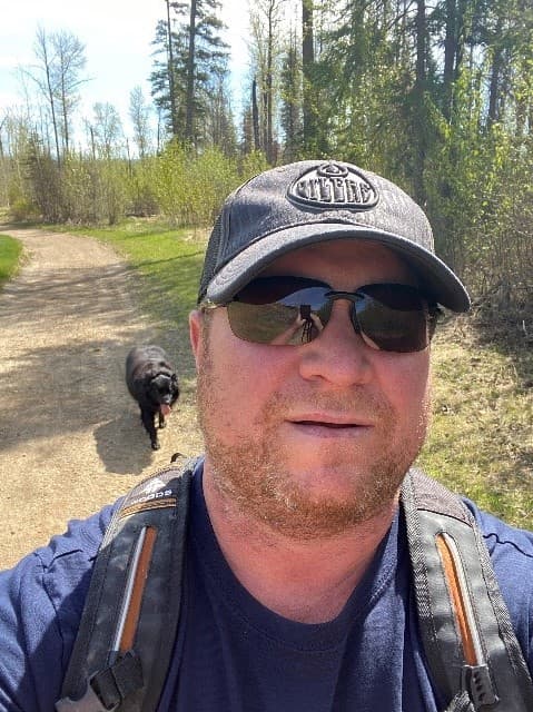 Jason Sinclair walking outdoors with black dog following him 