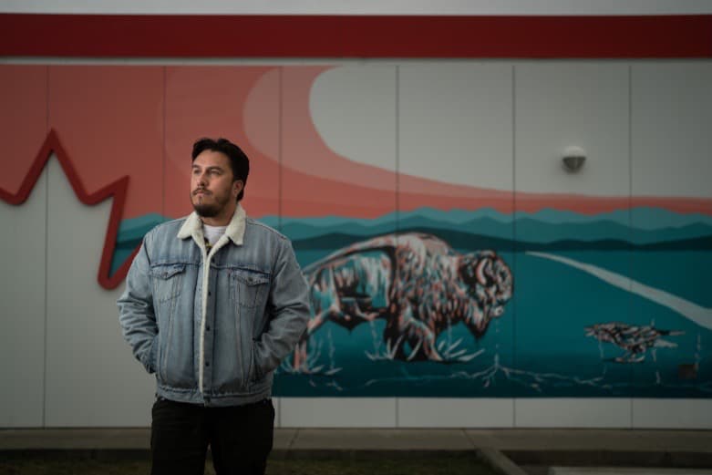 Keegan starlight en veste en jean debout devant sa fresque peinte sur une station-service Petro Canada