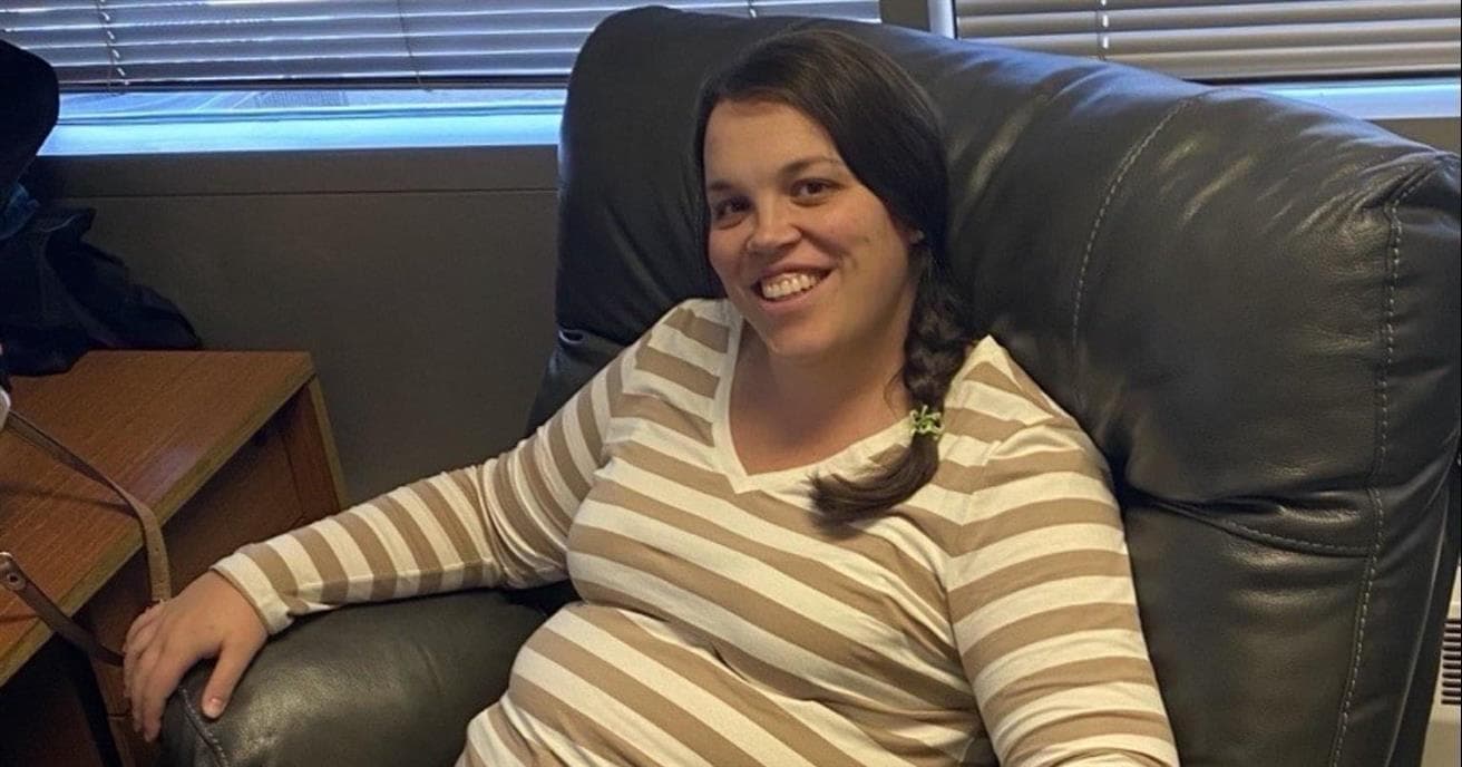 A pregnant woman sits in a comfortable chair in an office.