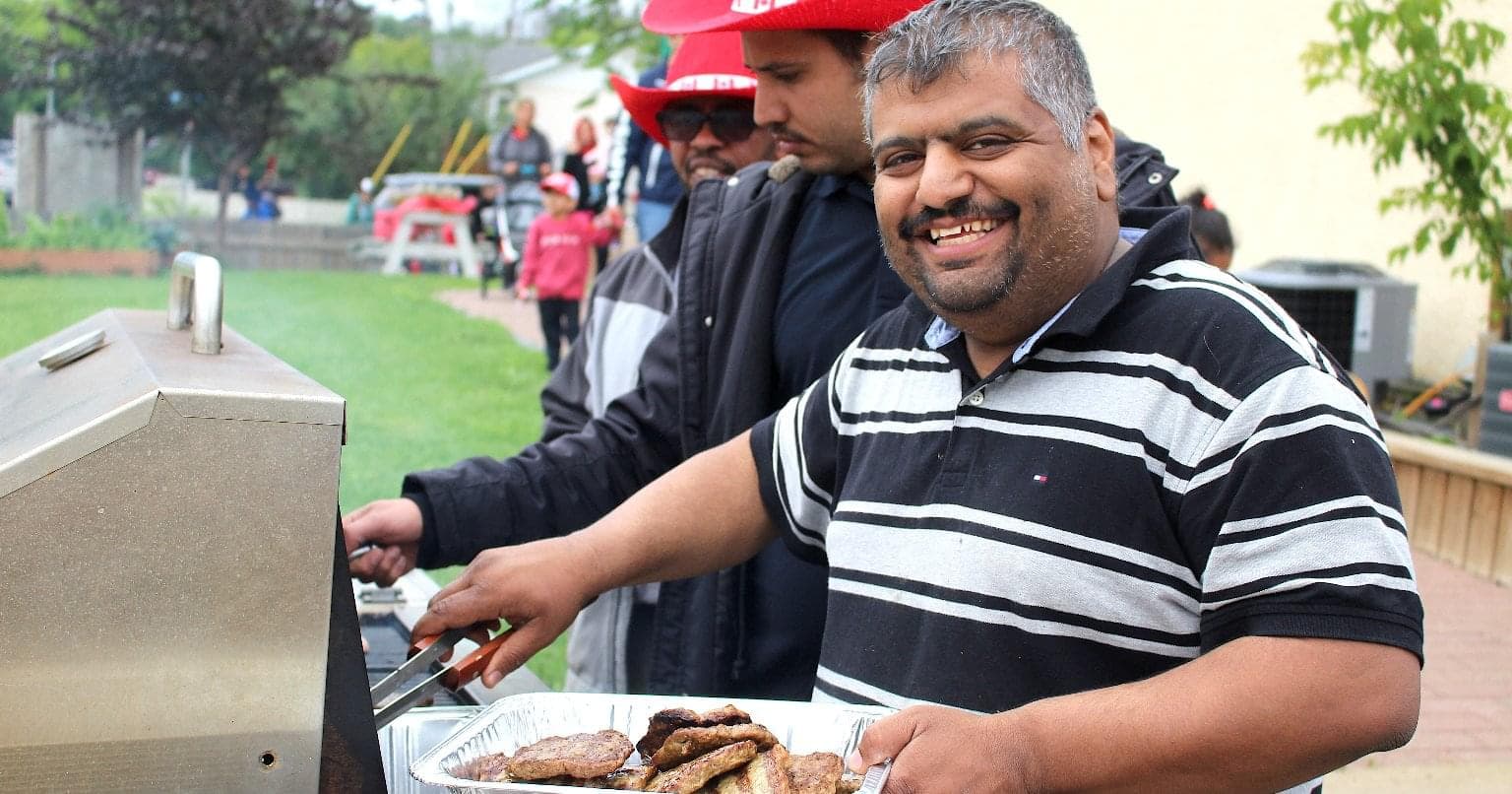 A man smiles at the camera while barbecuing burgers.
