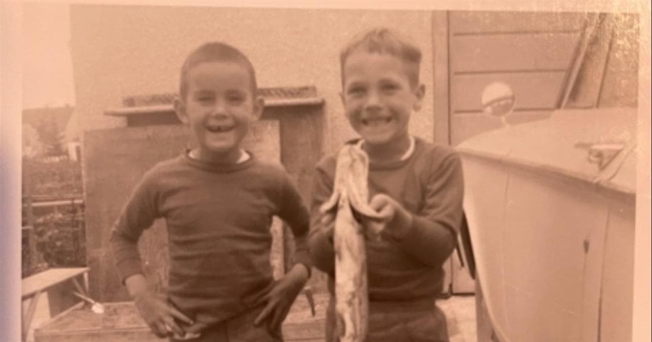 An old photograph of two young boys smiling. One boy is holding a fish.