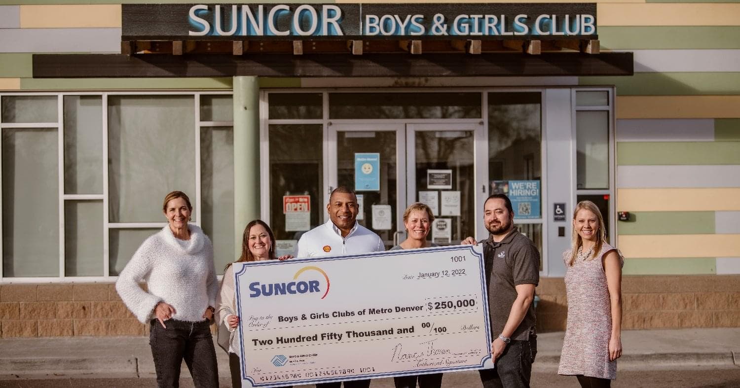 A group of six people hold a large check for $250,000 in front of a building. The check has the Suncor logo on it and is made out to the Boys & Girls Clubs of Metro Denver.