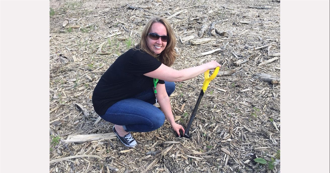 Anna crouching as she digs a hole with a shovel to plant trees after the 2016 wildfire in Wood Buffalo.