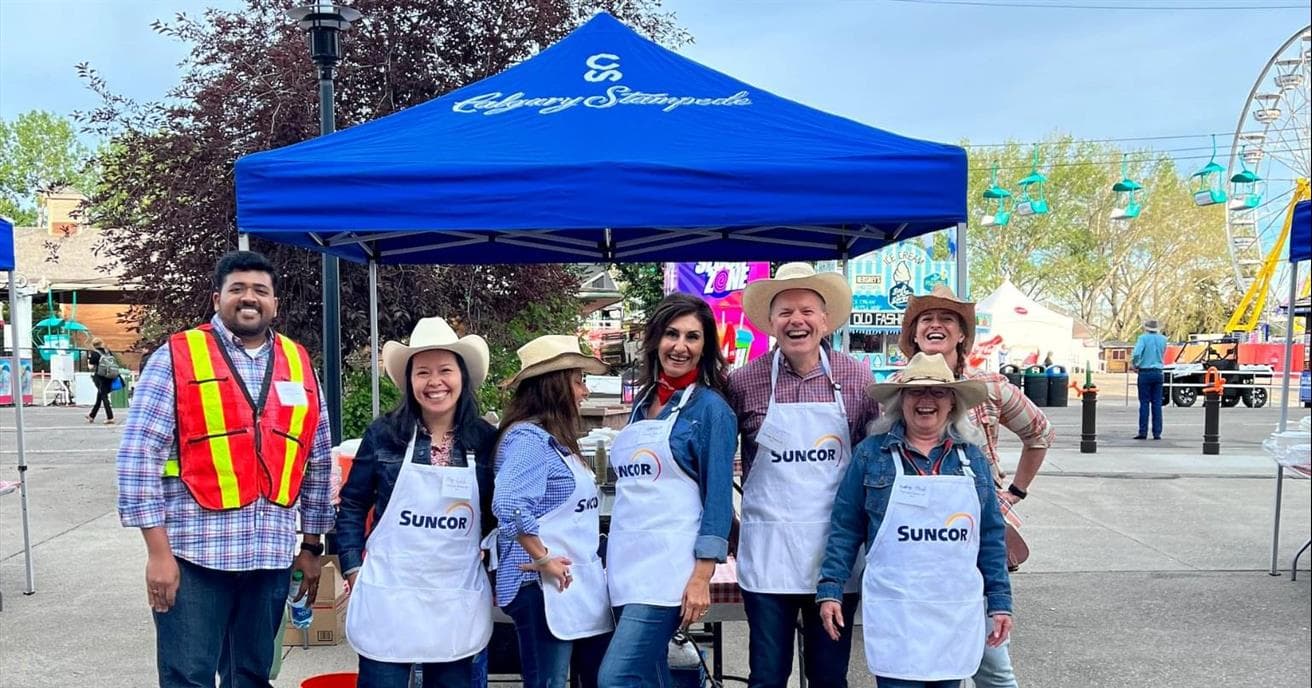 A group of people dressed in western wear laughing together in their Suncor aprons.
