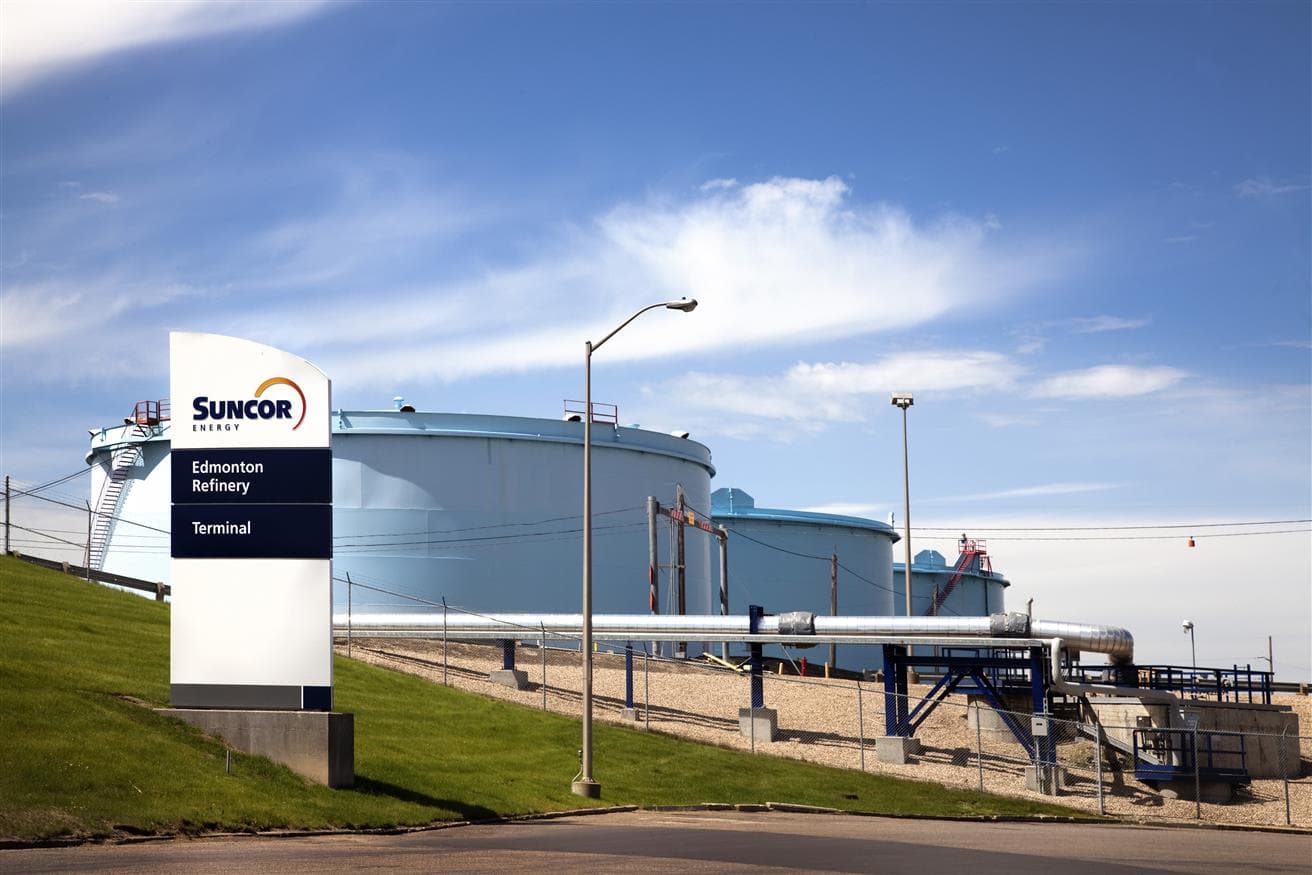 L'image a un fond de ciel bleu et la raffinerie d'Edmonton avec quatre réservoirs d'hydrogène et un panneau Suncor devant