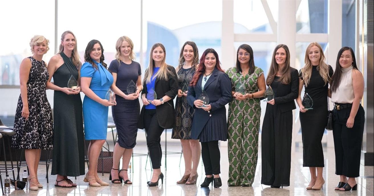 A group of 10 women stand in a line facing the camera. They are holding awards.