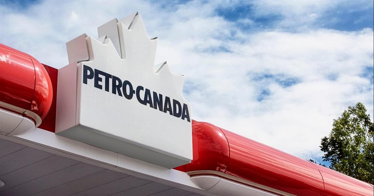 La marquise d'une station-service Petro-Canada. Il y a une affiche rouge et blanche arborant le logo de la feuille d'érable en blanc de Petro-Canada et un ciel bleu avec des nuages au-dessus.