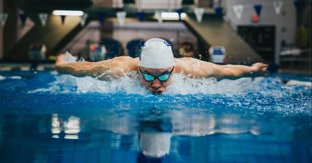 Une personne qui nage dans une piscine. Le nageur porte un bonnet de bain et des lunettes de natation de couleur blanche. L'eau est très bleue.