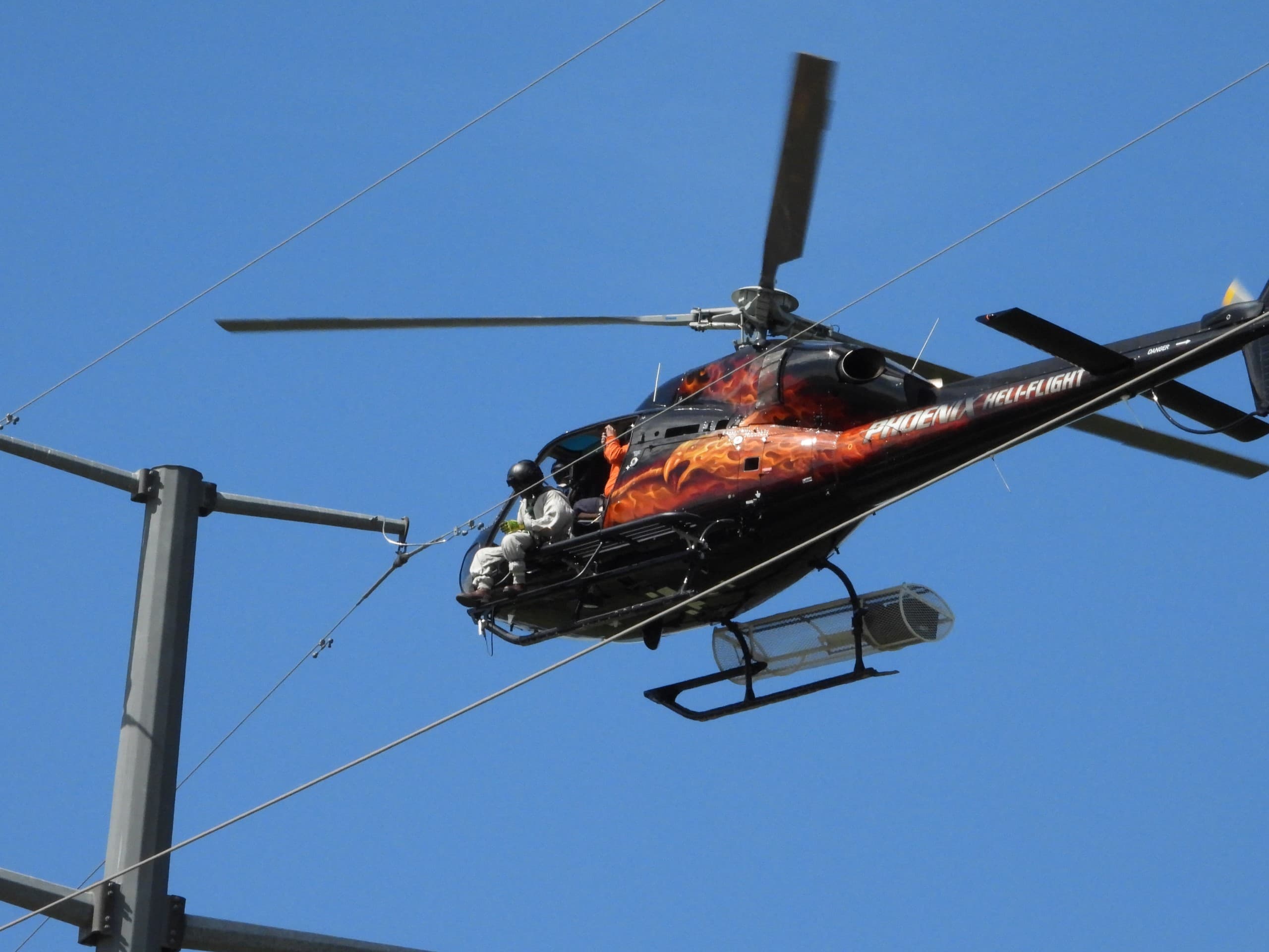 blue sky and helicopter close to high voltage transmission lines to install shield wires