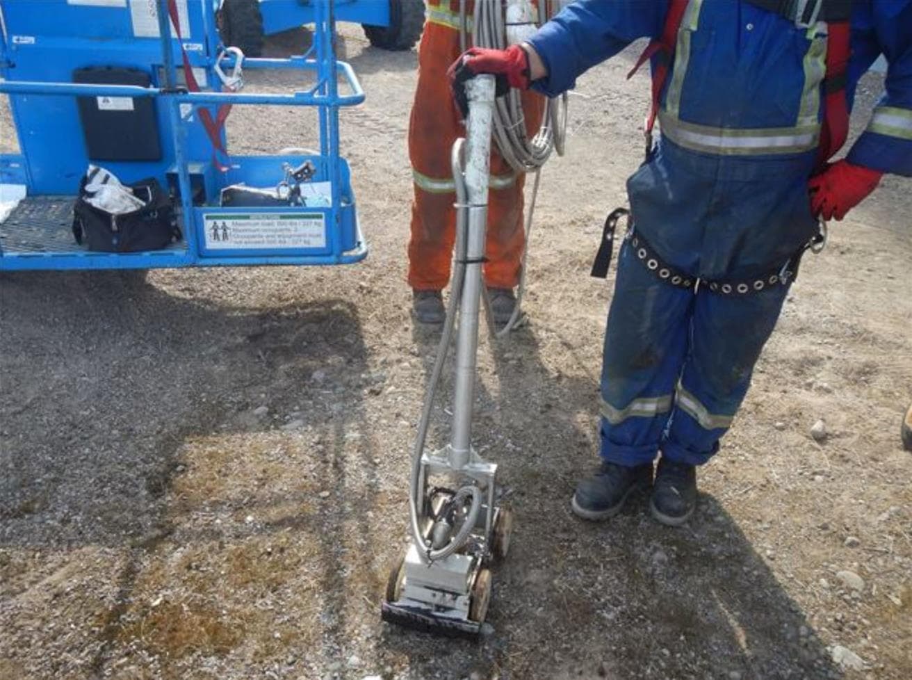 worker in full personal protective equipment holding the handle of the rimouski robot standing in a dirt path 