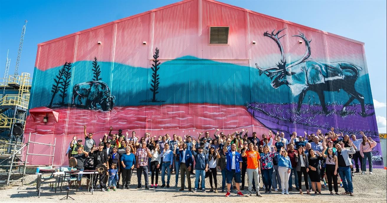 A group of people stand in front a building with a colourful mural painted on it. 