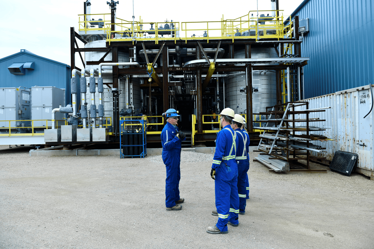 three individuals in personal protective equipment standing outside a blue facility 