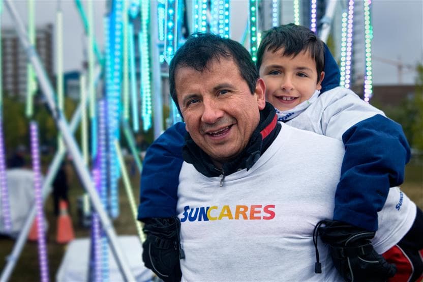 Man wearing a SunCares shirt smiling with a child on his back.