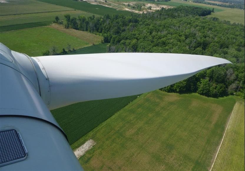 A photo taken from atop the nacelle of a wind turbine, looking down at a green field below