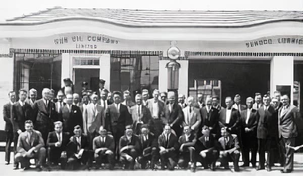 A group of employees for Sun Oil Company stand outside of a service station in the early 1900s. The majority are men wearing suits.