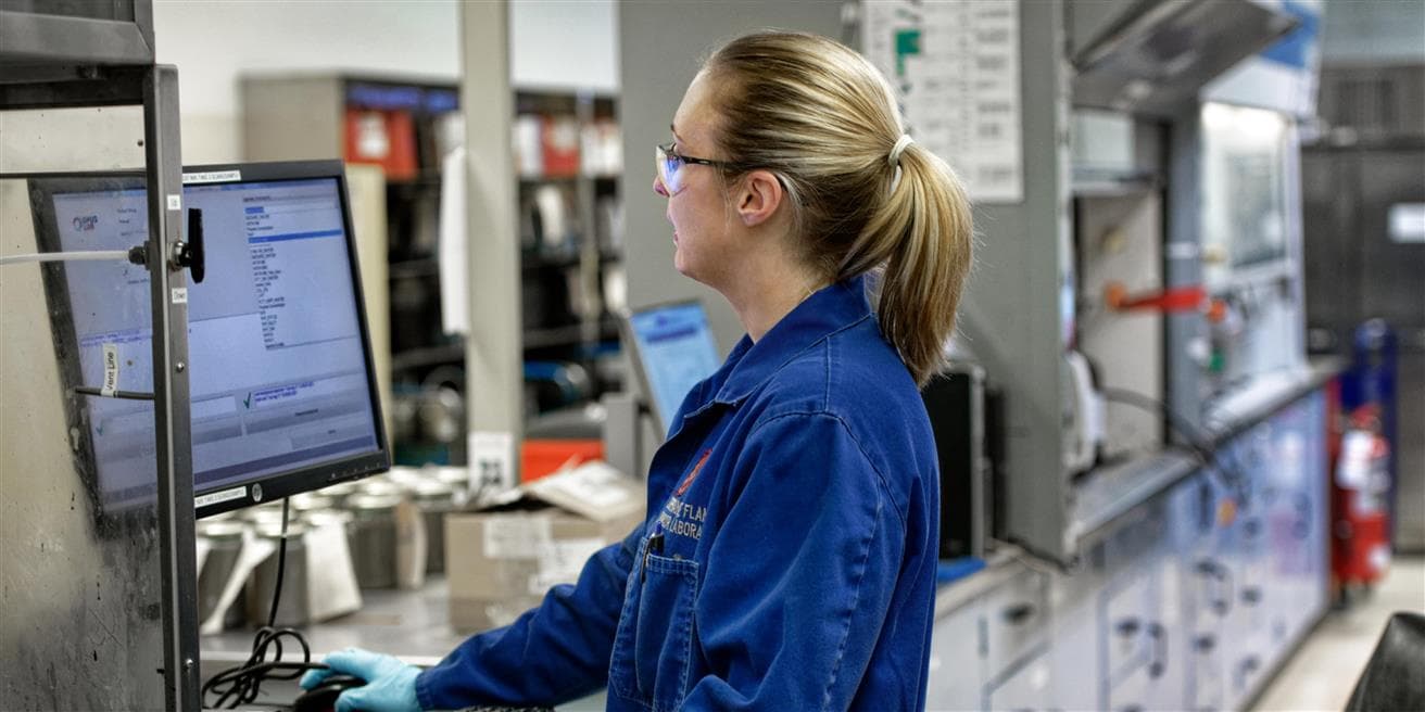 Une femme en combinaison bleue regarde un écran d'ordinateur dans un laboratoire.